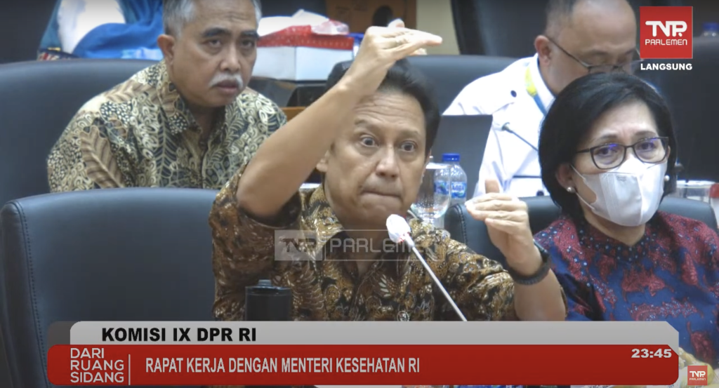 Health Minister Budi Gunadi Sadikin at the House of Representatives, gesturing to indicate the difference in status. Source: Screenshot from TV Parlemen via Project Multatuli