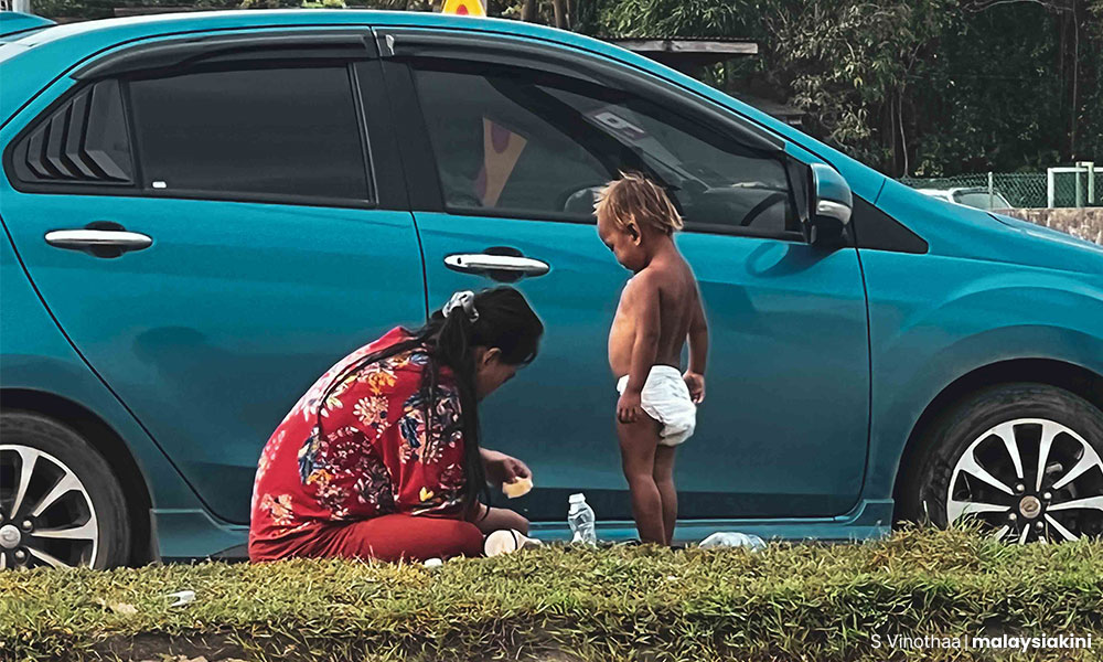 A woman making a bottle of milk for her child on a road divider. Photo: Malaysiakini