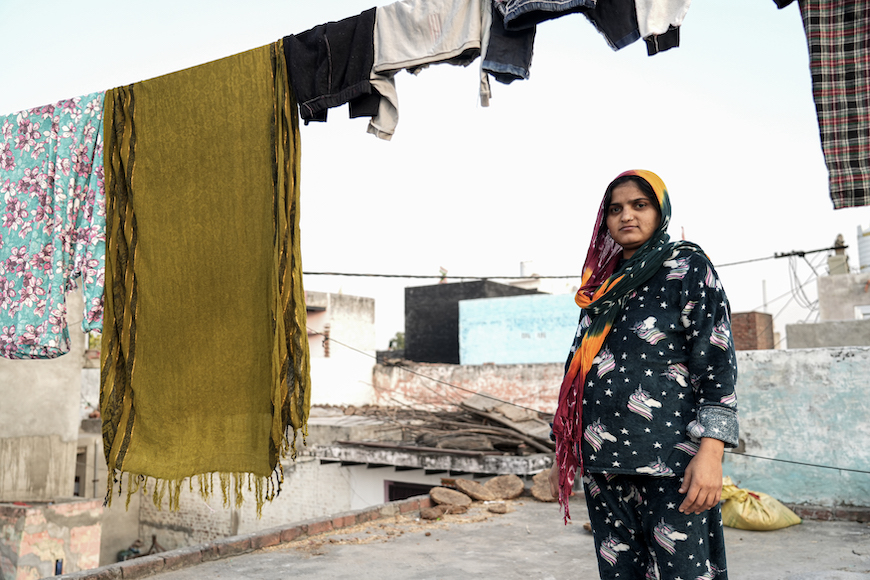 Anjeeli, 23, an eight-month pregnant resident of Uncha Amirpur, look at the camera while standing on a terrace, with hanging clothes in the forefront. Photo: Suhail Bhat