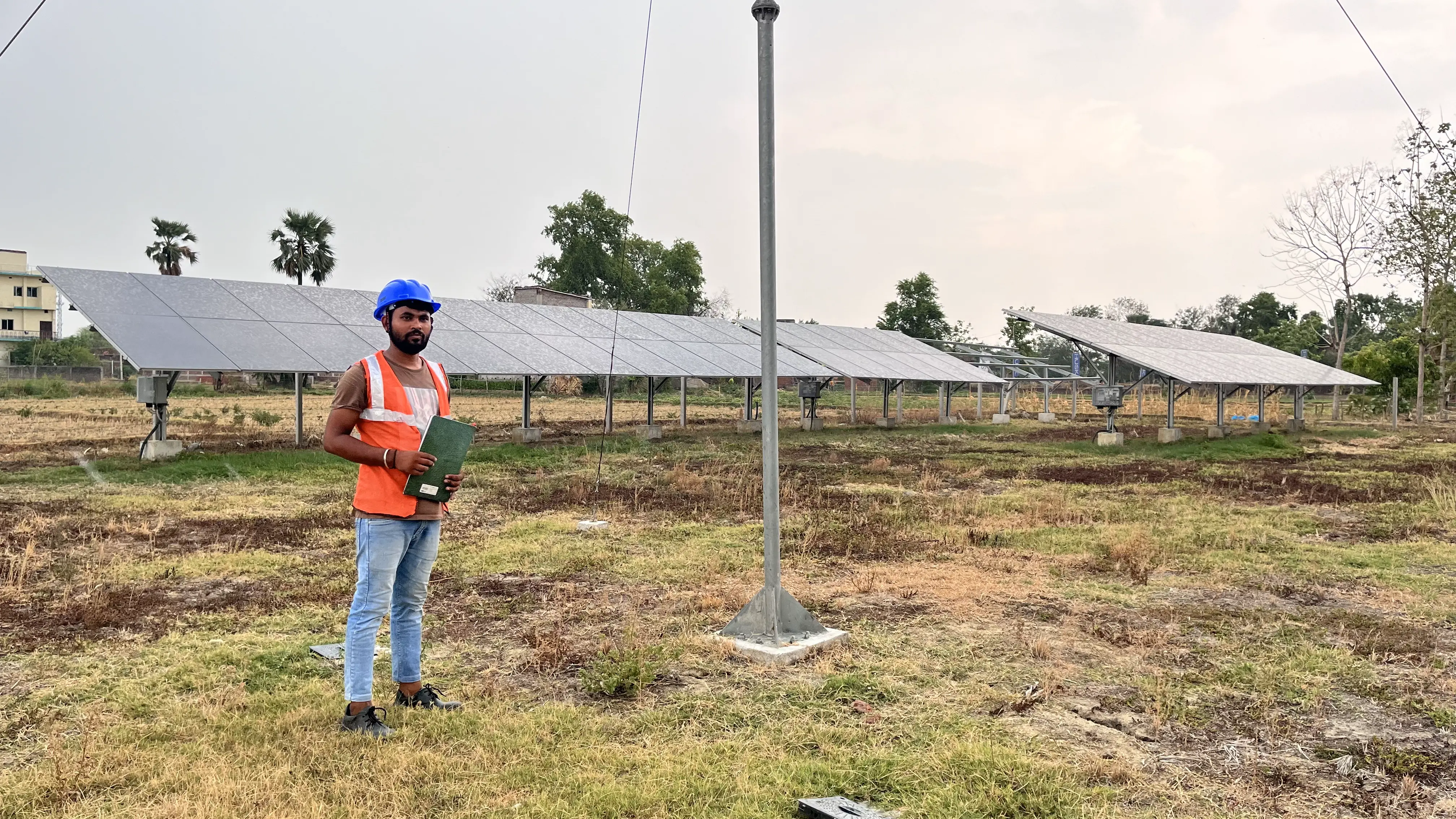 Pintu Kumar, in an orange construction vest, poses with solar panels in Gaya district, Bihar. Photo: Sneha Richhariya