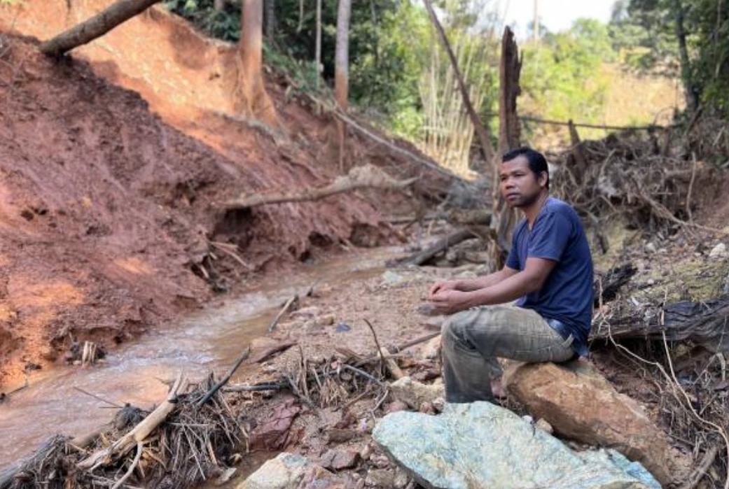 Alai Angah sits by the river bank which has been tainted a rusty red from iron tailing. Photo: S Vinothaa/Malaysiakini