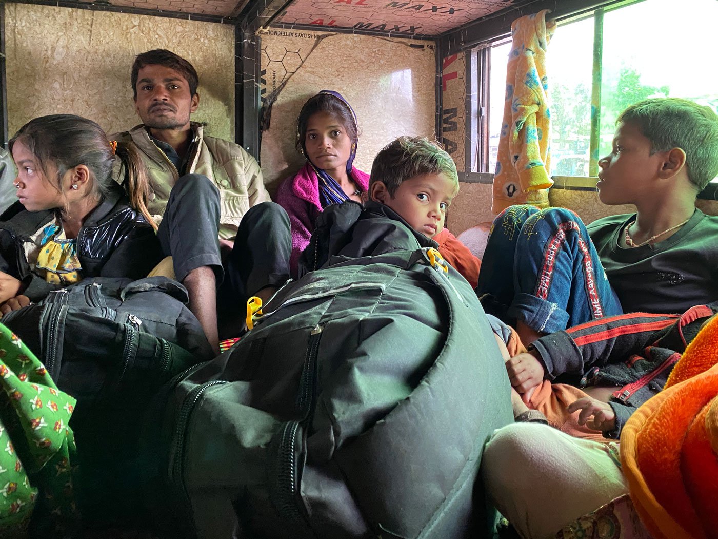 At the Timeda bus stand in Kushalgarh, roughly 10-12 busses leave every day for Surat and big cities in Gujarat carrying labourers – either alone or with their families – looking for wage work. Image shows a couple with young children sitting at the back of a bus. Photo: Priti David/PARI