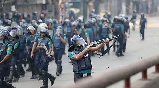 Police officers with protective gear patrol the streets at Malibagh in Dhaka during the 2024 protests. In center frame, a police officer points his gun at something off screen. Photo: Suvra Kanti Das/Prothom Alo