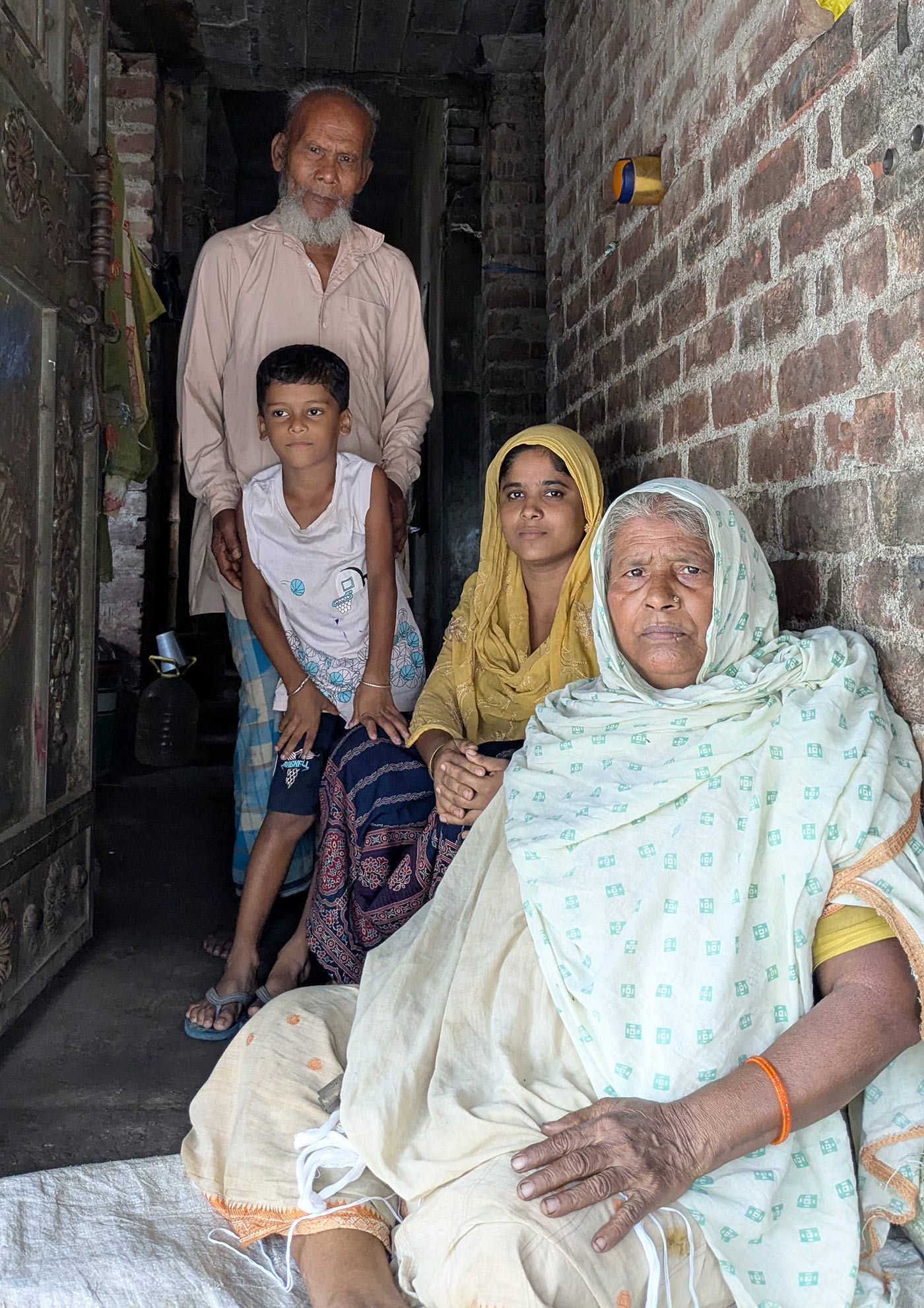 আটক পরিযায়ী শ্রমিক আইনাল হকের স্ত্রী শিউলি বিবি, তাঁদের ছেলে, মা মদিনা বিবি আর বাবা মইনুল শেখ, ভগবানগোলার ১ ব্লকের ডিয়ার জালি বাগিচা গ্রামে নিজেদের বাড়িতে।Photo: Anirban Dey/PARI