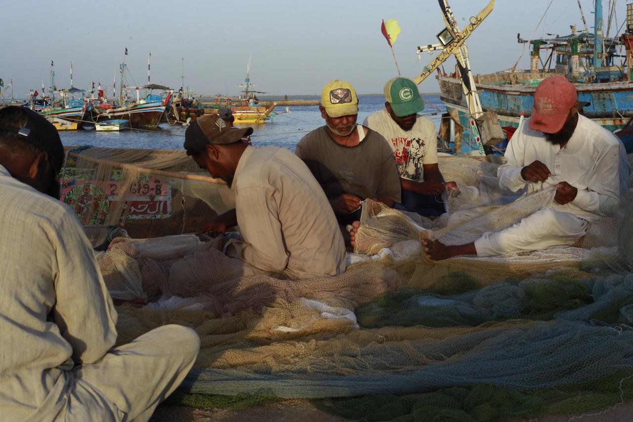 Image shows men mending nets in Ibrahim Hyderi.